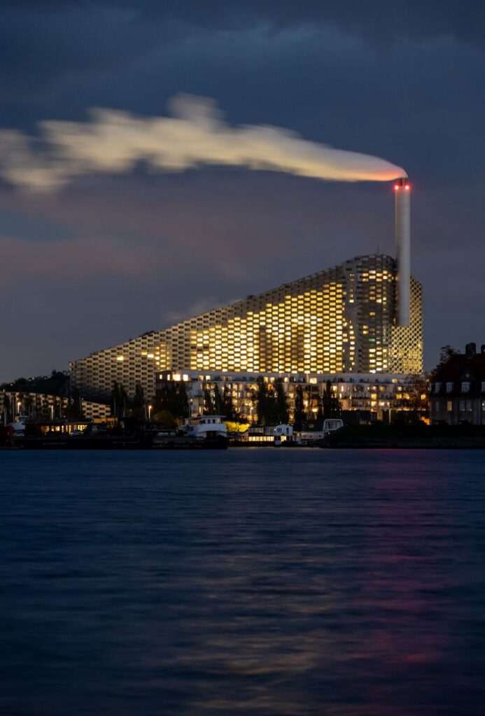 Stunning night view of Amager Bakke power plant emitting smoke against a moody sky in Copenhagen, Denmark.