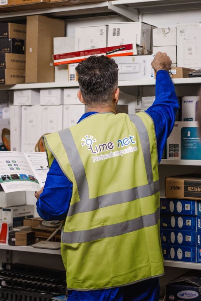 Man sorting inventory in Erbil warehouse, wearing reflective vest, standing back view