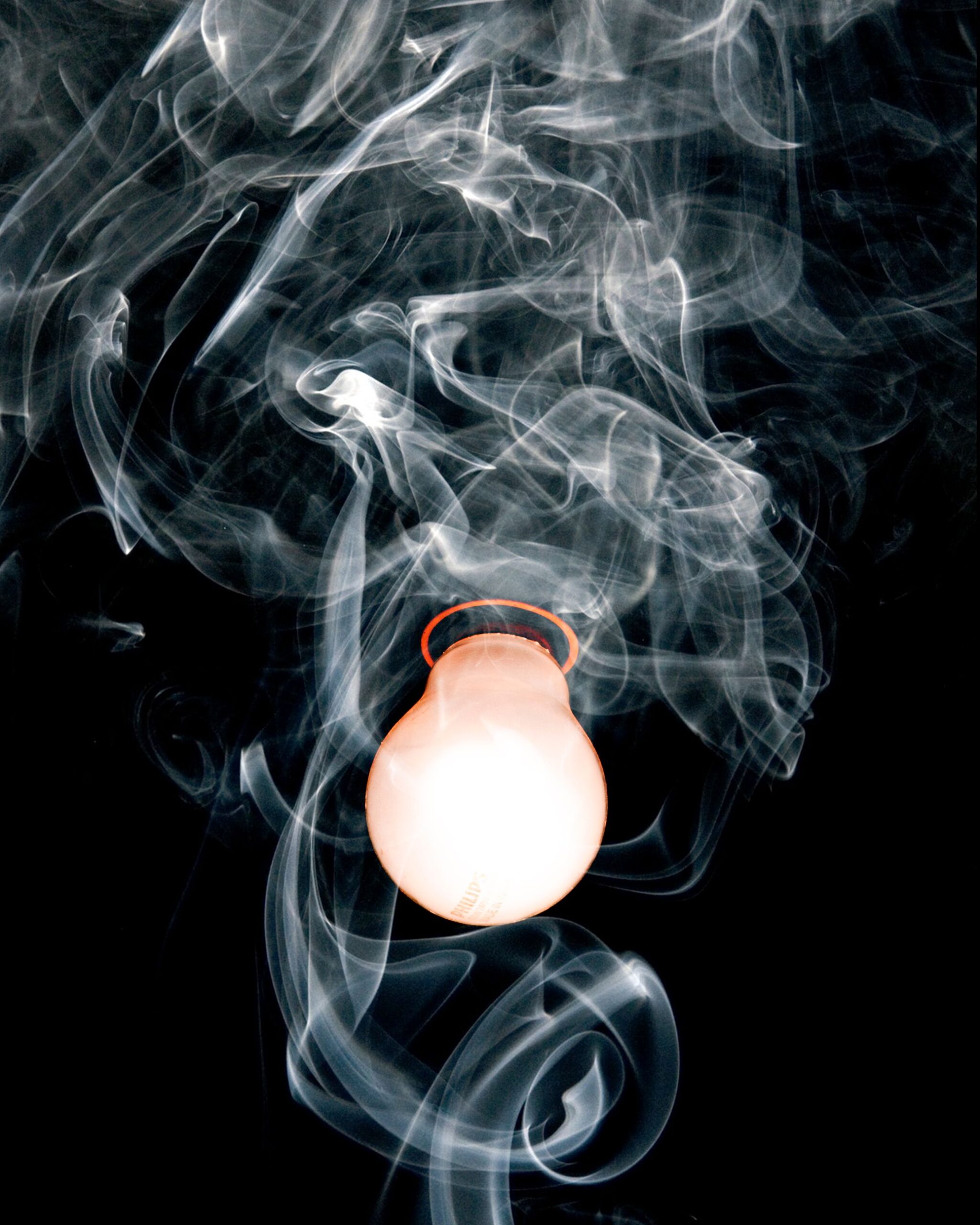 Close-up of a glowing light bulb surrounded by swirling smoke against a dark background.