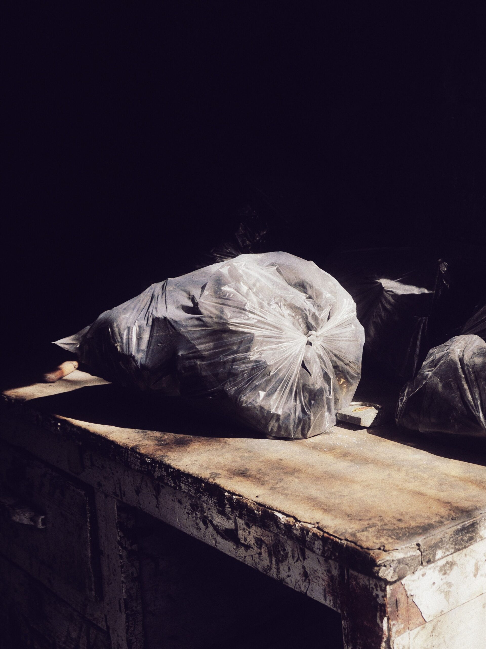 Dramatic photo of trash bags on a rustic table with deep shadows.